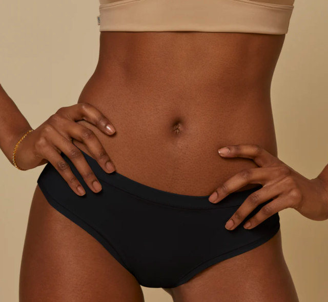 the torso of a woman standing in black brief underwear with hands on hips